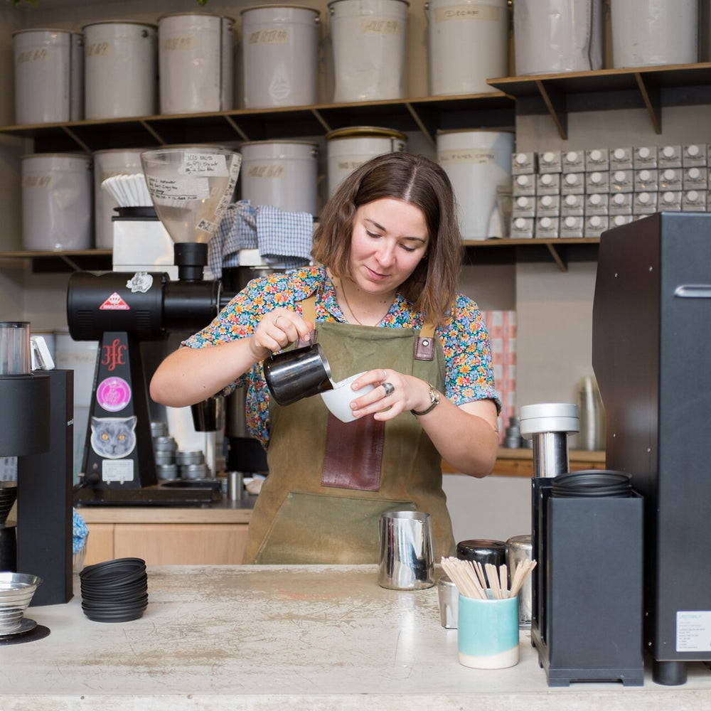 Barista pouring latte art at Rosslyn Coffee, with an Übermilk ONE on the bar